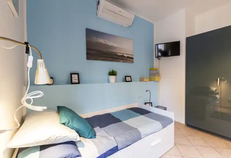 A bright, neatly styled single bedroom with a daybed, decorative cushion, wall art and a glossy wardrobe — ideal for a short-term rental or guest room.