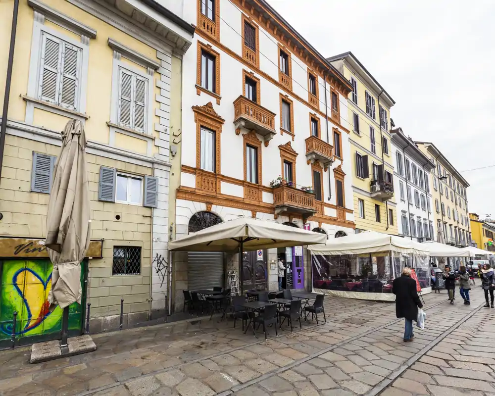 Street-side outdoor terrace with tables and umbrellas in front of classic multi-story buildings; ideal for showcasing an exterior café area and pedestrian-friendly historic street.