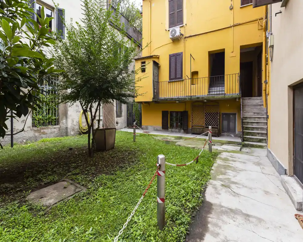 Sunny courtyard with a grassy area, small tree and surrounding apartment façades; suitable for a listing highlighting a private communal garden or inner courtyard.