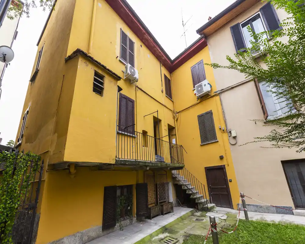 Exterior courtyard area of a multi-storey residential building with yellow-painted walls, external staircase, balconies and small grass patch.