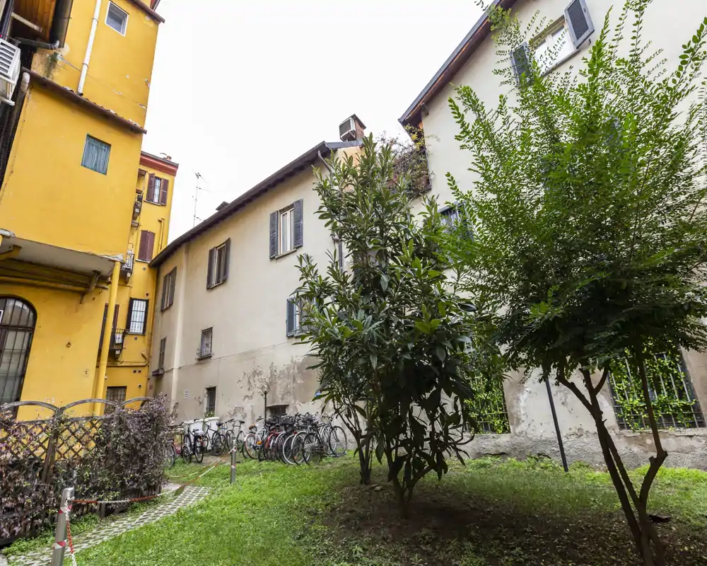 Private courtyard with grass, small trees and a bicycle rack beside traditional apartment buildings — a quiet outdoor space suitable for residents.