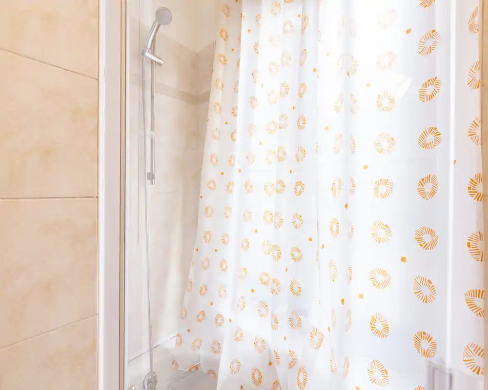 Bright, clean bathroom shower with patterned shower curtain and chrome hand shower; neutral tiles and soft lighting create a fresh, tidy look.