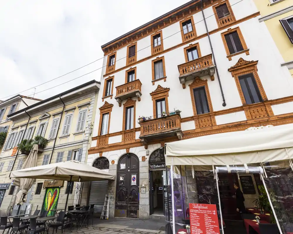 Street-front exterior with outdoor café seating in front of a multi-story building featuring decorative balconies and awnings.