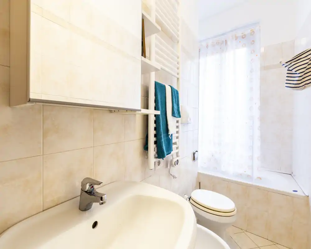Bright, tidy bathroom with sink, bathtub and toilet; light tiles and a towel rail with colorful towels create a pleasant, clean atmosphere.