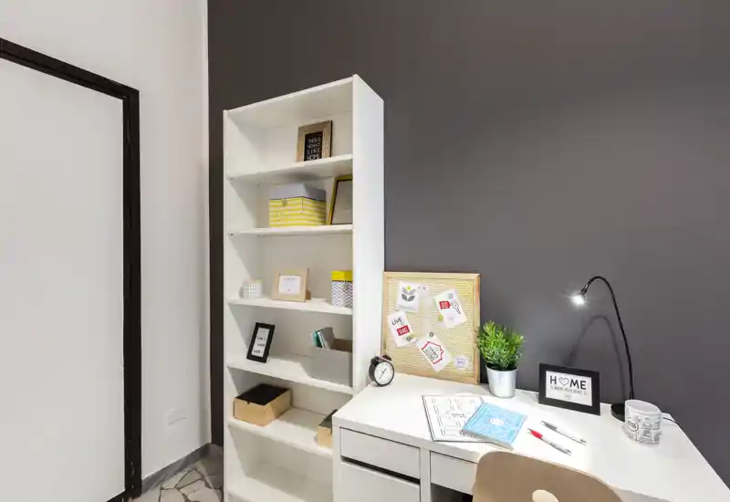 Angolo home office luminoso e ordinato con scrivania bianca, scaffale, bacheca e lampada da scrivania — perfetto per lavoro o studio concentrato.