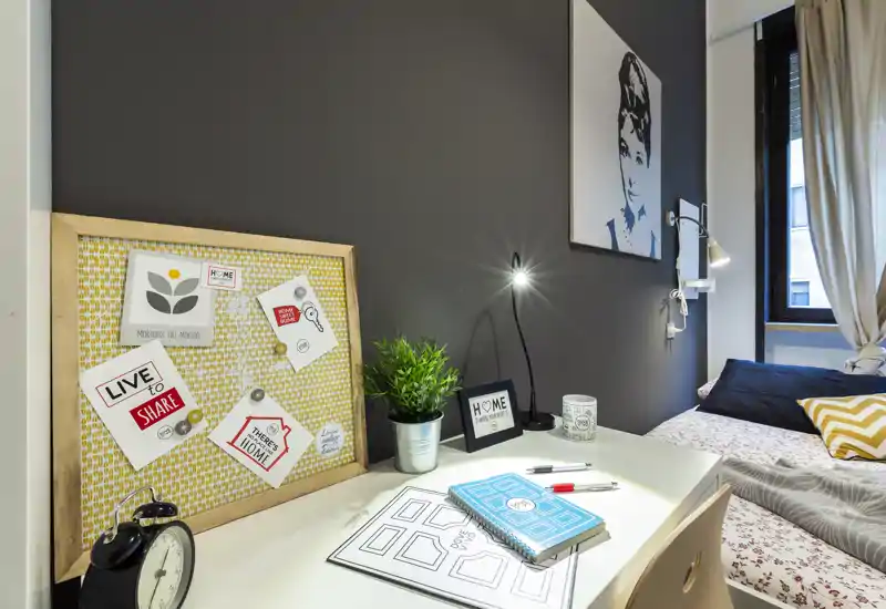 Angolo camera luminoso e stiloso con scrivania, bacheca decorativa e letto ben rifatto — ideale per studio e riposo.