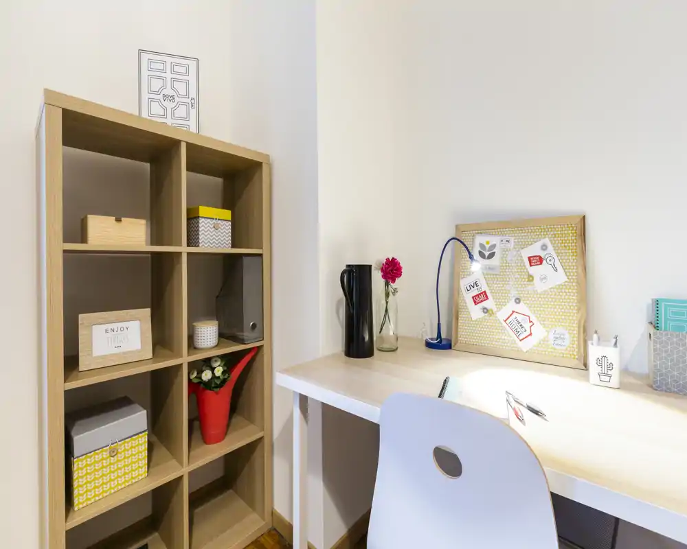 Bright, tidy study corner with a light wood desk, pinboard, decorative vase and organized shelving — ideal for focused work or reading.