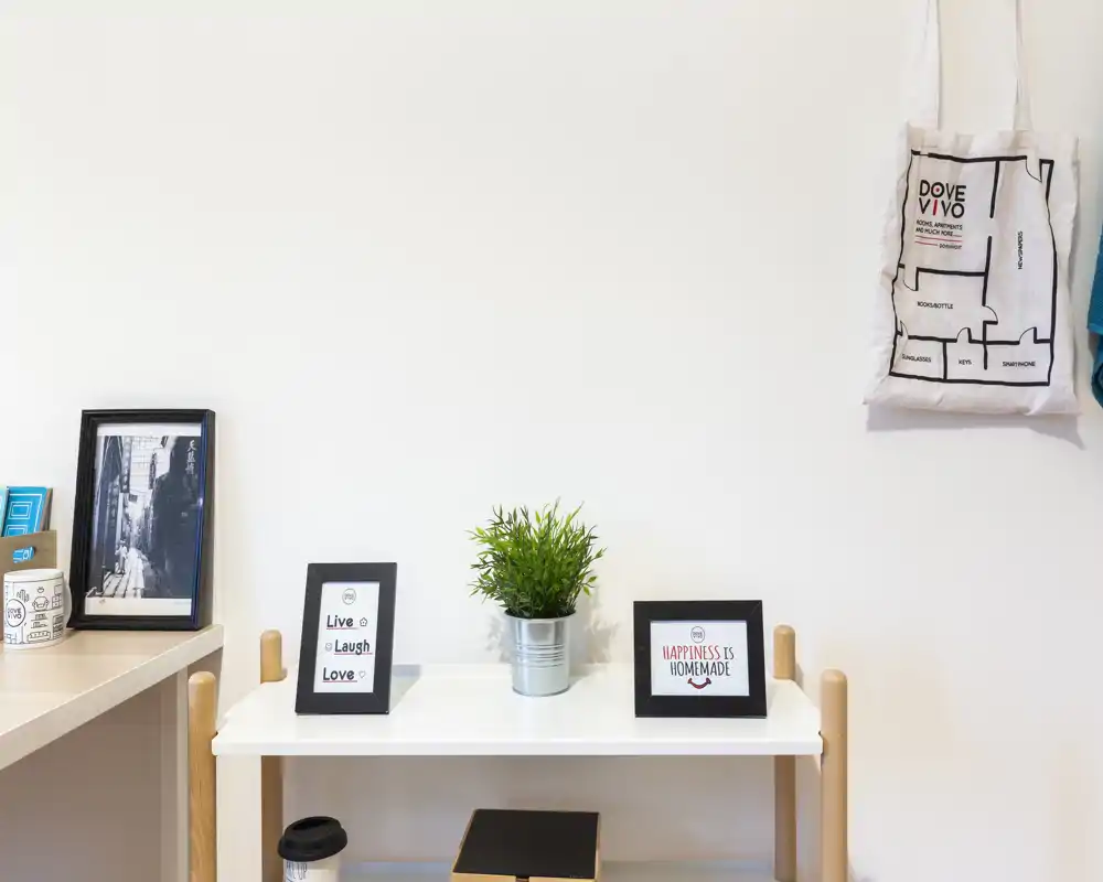 Neat entry/console area with decorative frames, a small plant and hooks for bags — bright and minimal styling suitable for a welcoming entrance.