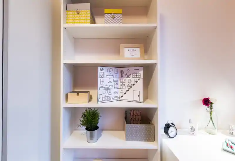 Area con scaffalatura luminosa e curata con scatole decorative, una piccola pianta e una sveglia su una superficie vicina — dettagli ordinati che creano un angolo accogliente in una zona giorno.