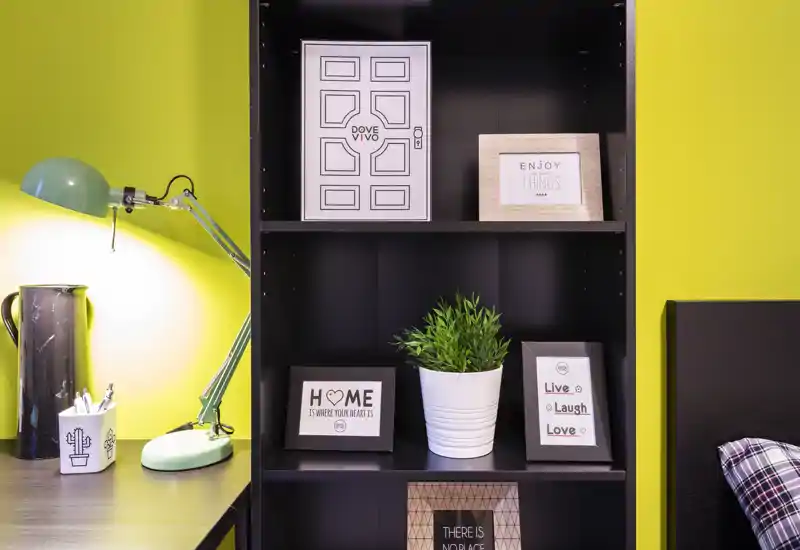 Mensola decorativa e angolo scrivania con lampada verde, cornici con citazioni e una pianta in vaso—dettaglio luminoso e moderno perfetto per annunci di stile.