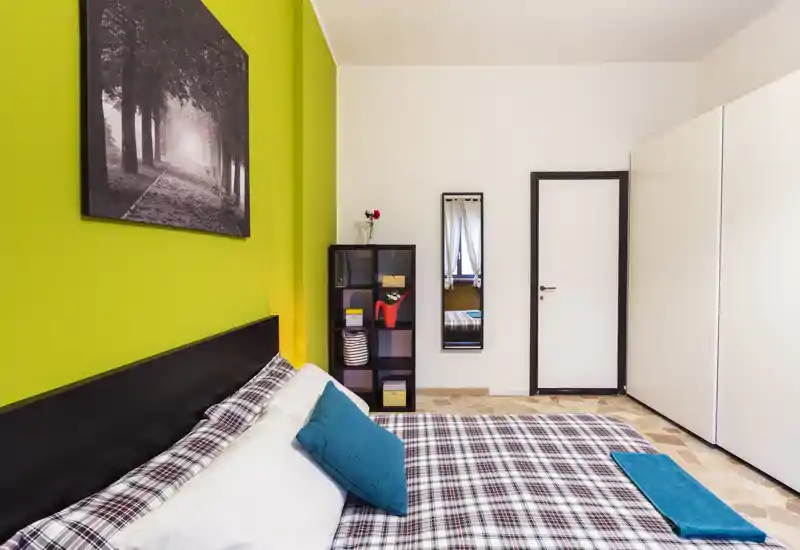 Bright, modern bedroom with a comfortable double bed dressed in checked linens, teal cushions and coordinated throw; green accent wall and tasteful decor create a fresh, welcoming atmosphere.