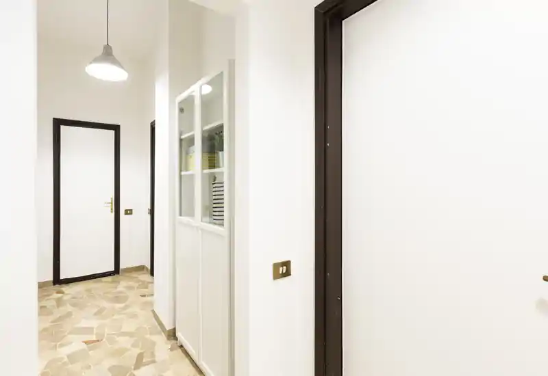 Ingresso luminoso e minimale con pavimento in piastrelle, pareti bianche e lampada a sospensione — area d'ingresso funzionale con scaffalatura integrata e porte interne.