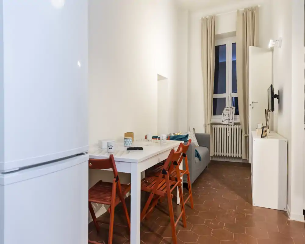 Area giorno compatta e ben arredata con divano, tavolo da pranzo e finestra luminosa — perfetta per un piccolo appartamento.