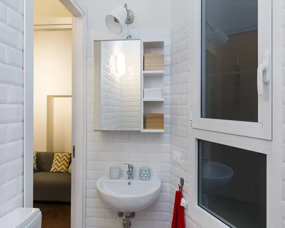 Bagno compatto e moderno con piastrelle bianche a metrò, lavabo a parete e mobiletto con specchio; luminoso, pulito e ben illuminato, perfetto per annunci di affitto.
