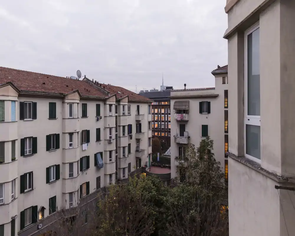 Vista del patio urbano desde una ventana que muestra edificios colindantes, tejados y un pequeño patio común — luz suave del atardecer y carácter urbano.