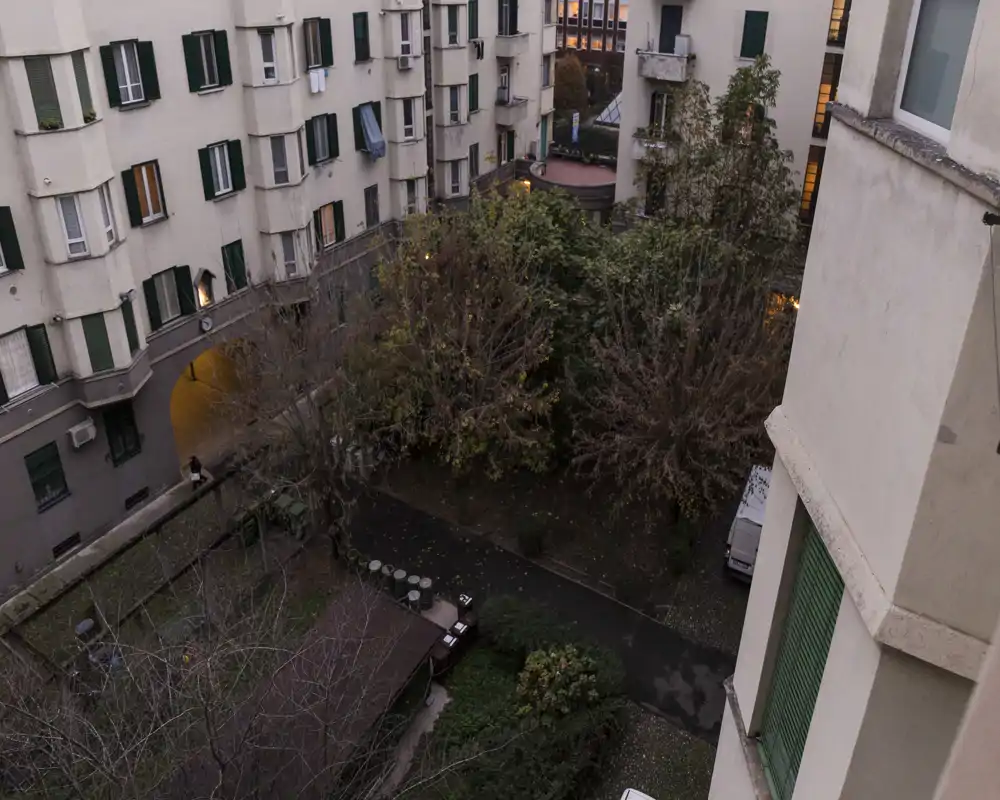 Vista de un patio interior entre edificios con árboles, caminos y algunas zonas para sentarse — adecuado para describir un espacio exterior comunitario.