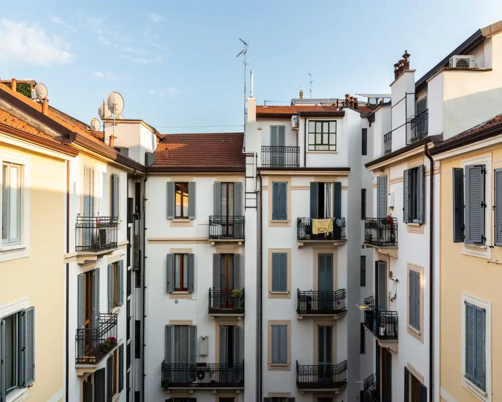 Vista exterior de un patio residencial con edificios de varias plantas y pequeños balcones, captada a la luz del día — ideal para mostrar fachadas y detalles de los balcones.