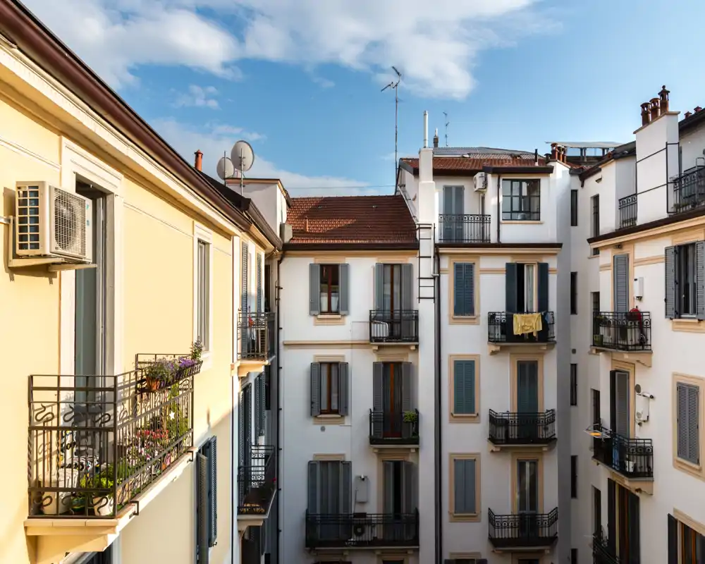 Vista luminosa del patio con varios balcones, barandillas con macetas y cielo despejado — apropiada para destacar la zona exterior del anuncio.