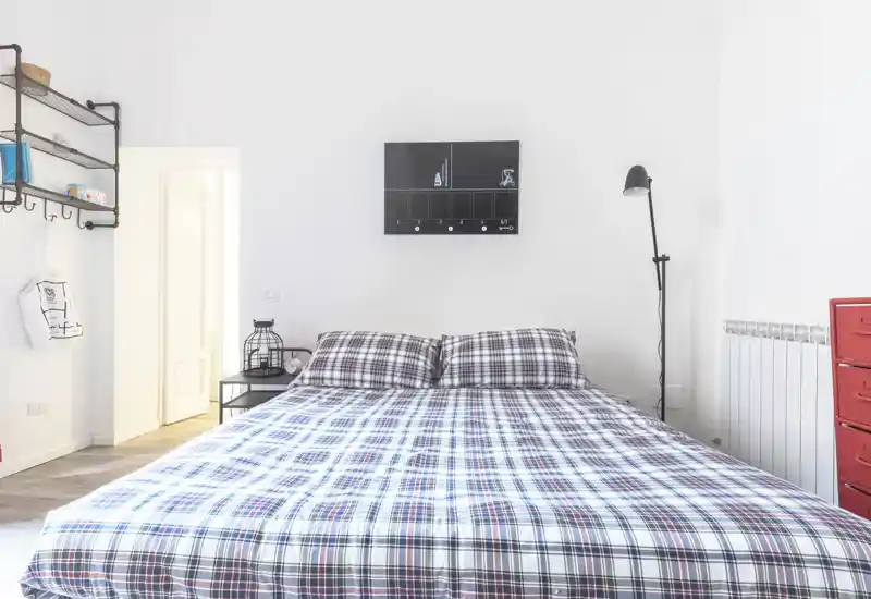 Camera da letto luminosa e minimalista con un ampio letto matrimoniale coperto da una trapunta a fantasia, lampada da comodino e mensole semplici: ariosa e ben curata per gli annunci.