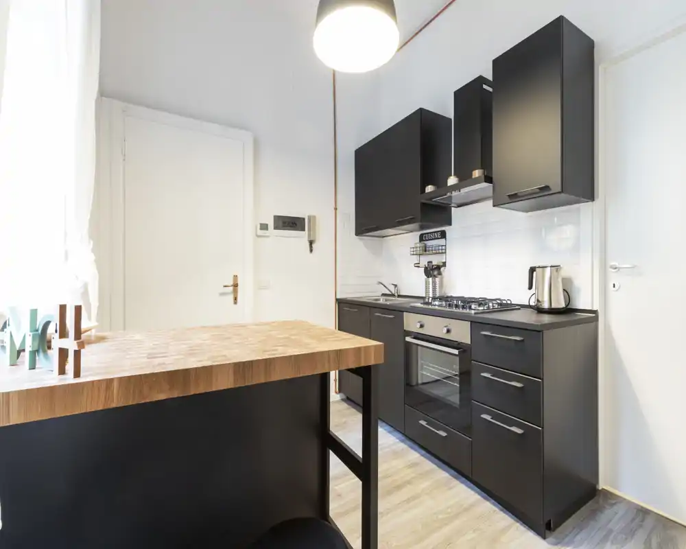 Cucina moderna compatta con mobili neri, forno e piano cottura a gas integrati e un bancone in legno. Spazio luminoso e ben organizzato ideale per appartamenti piccoli.