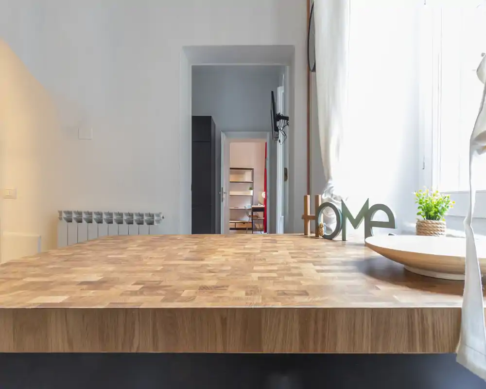 Veduta del piano cucina con un ampio top in legno, piccoli elementi decorativi e luce naturale proveniente dalla finestra.