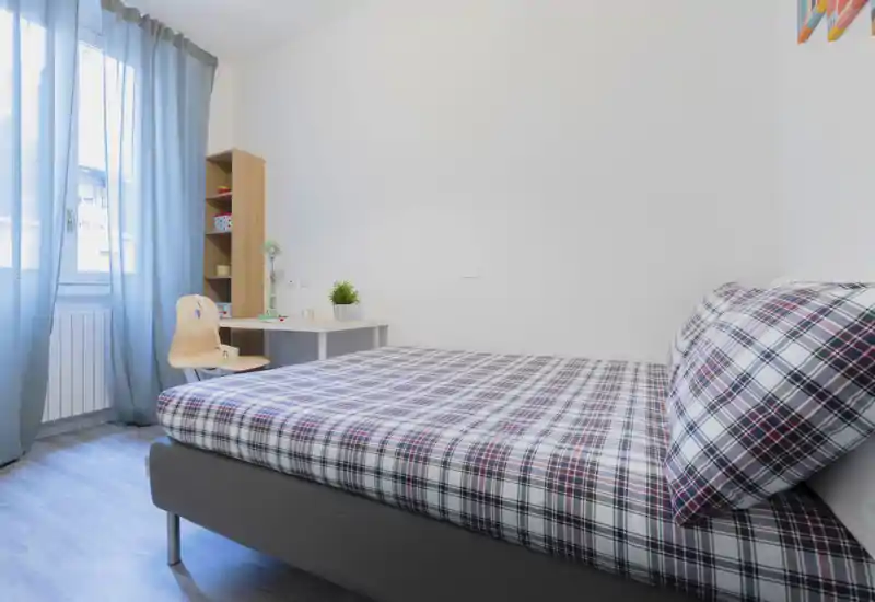 Bright, tidy single bedroom with patterned bedding, a small study desk and natural light from a window—ideal for a comfortable short-term stay.