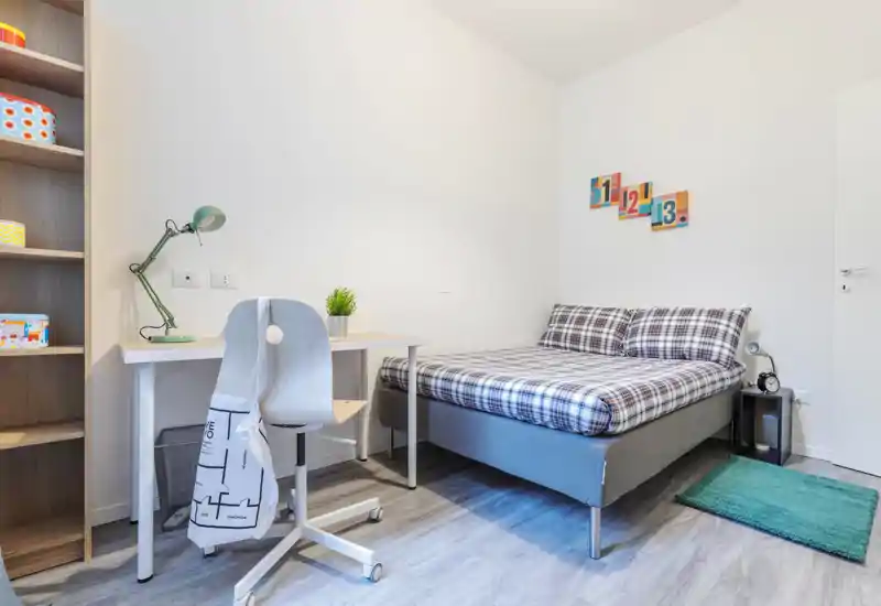 Bright, modern bedroom with a double bed dressed in checkered linens, a small bedside table, and a compact desk ideal for study or remote work.