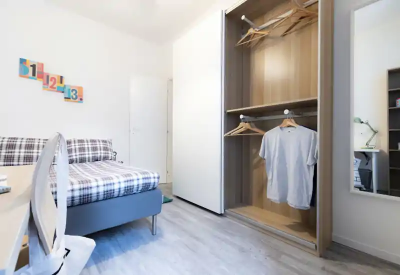 Bright, modern bedroom with a neatly made single bed, open wardrobe with hangers, and a minimalist desk area — ideal for a rental listing highlighting tidy, functional sleeping space.
