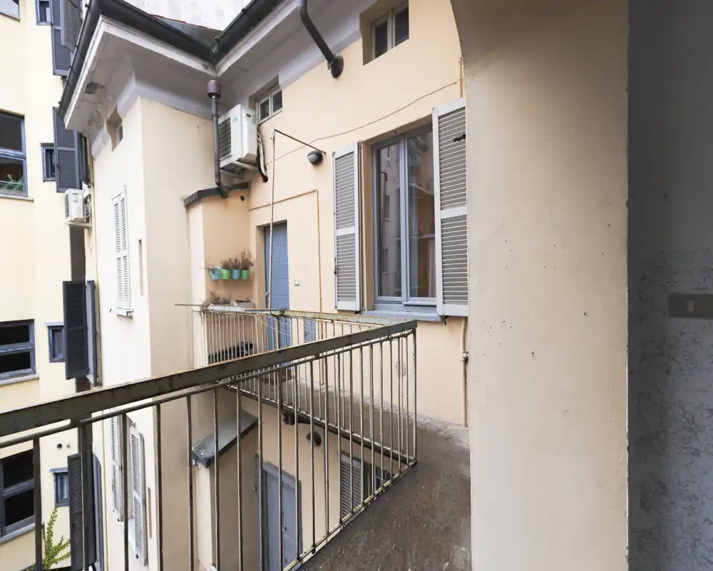 Small external balcony overlooking an inner courtyard, with metal railings, shuttered windows and wall-mounted planters — suitable for a compact outdoor area.