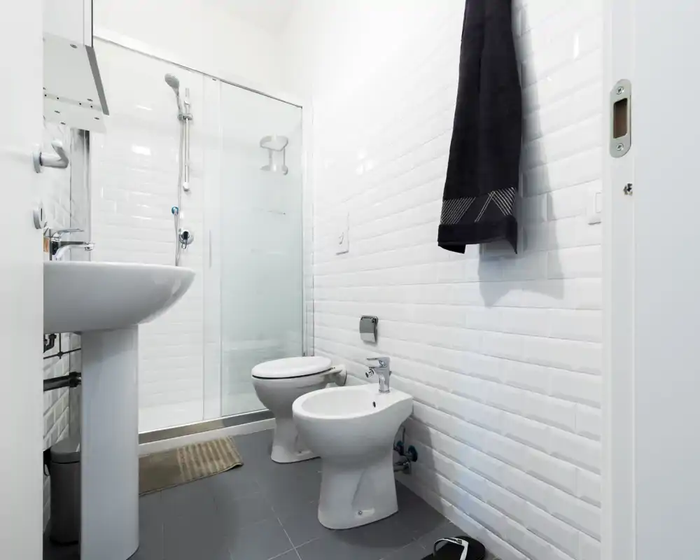 Bright, modern bathroom with white subway tiles, pedestal sink, shower with glass door, toilet and bidet—clean and functional layout ideal for a rental listing.