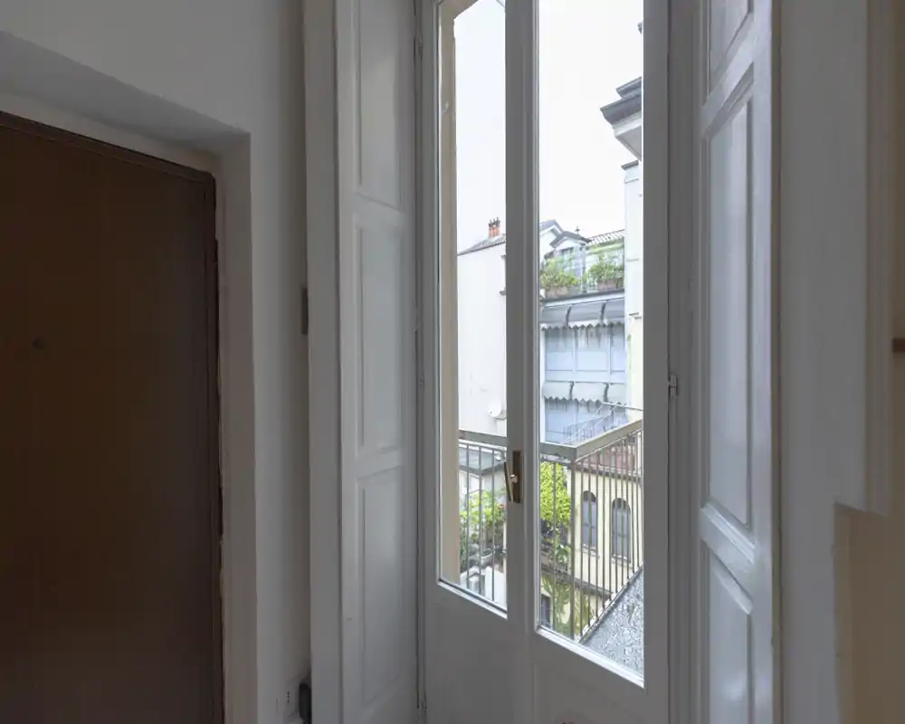 Small entrance/hallway with a wooden door and a tall glass door leading to a balcony, letting in natural light and offering an exterior view.