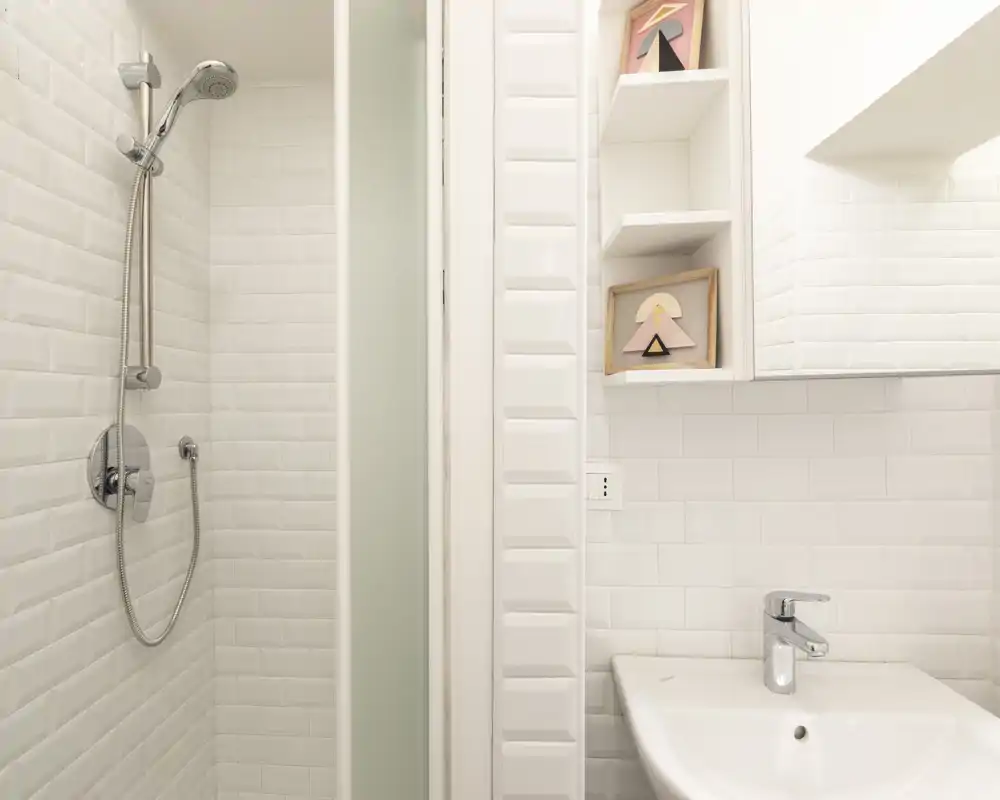 Clean, modern bathroom with a tiled shower and a white sink; minimalist shelving and chrome fixtures create a bright, sanitary space.