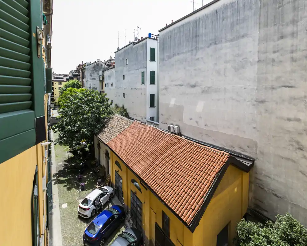 Sunny courtyard view with tiled roof, parked cars and mature trees — a bright, private outdoor area visible from the building windows.