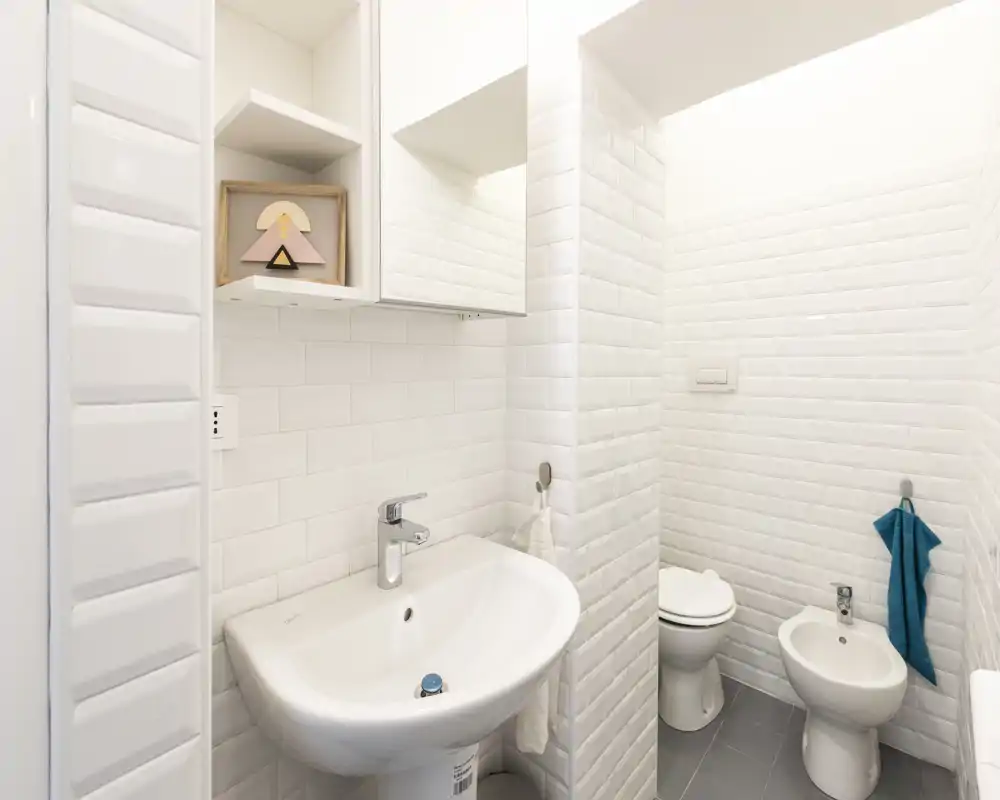 Bright, modern bathroom with white subway tiles, a wall-mounted mirror cabinet, sink, toilet and bidet; clean and well-lit space suitable for guests.
