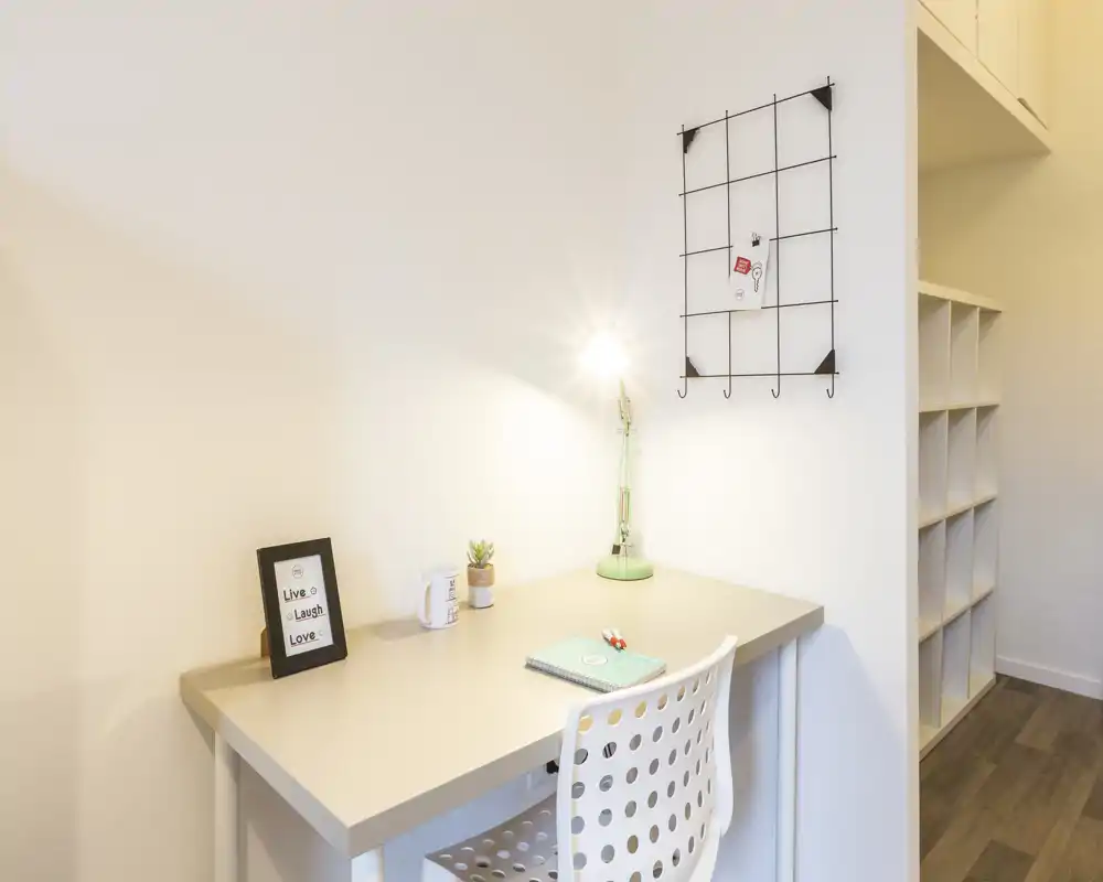 Pequeño espacio de trabajo luminoso con escritorio sencillo, silla perforada, lámpara de escritorio y decoración minimalista — ideal para estudiar o trabajar desde casa.