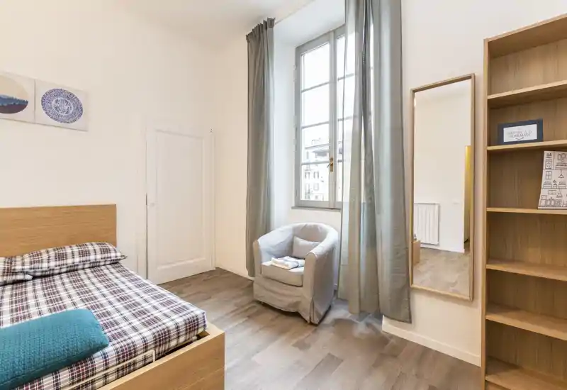 Dormitorio luminoso y bien decorado con cama de madera, butaca junto a la ventana y tonos neutros, perfecto para fotos de alquiler.