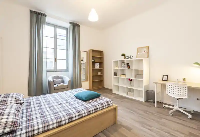Dormitorio luminoso y moderno con una gran ventana, ropa de cama a cuadros, un sillón cómodo y un escritorio ordenado — ideal para una persona o invitados.