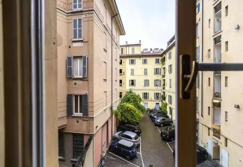 Vue depuis la fenêtre sur une petite cour intérieure avec des voitures garées entre des immeubles résidentiels ; photo pratique pour situer le bien.