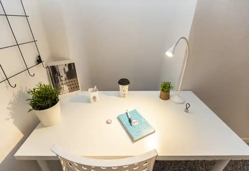 Bureau blanc minimaliste avec lampe, plantes en pot, un carnet et un gobelet de café à emporter — un coin bureau lumineux et soigné.