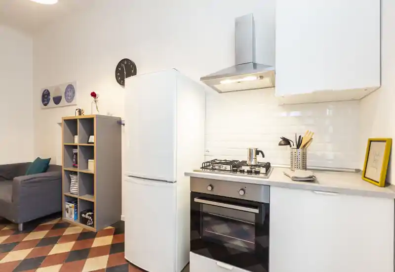 Coin cuisine moderne et compact avec plaque à gaz, four encastré et réfrigérateur indépendant ; meubles blancs, crédence en carreaux subway et décor soigné la rendent lumineuse et accueillante.