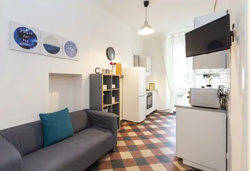 Espace de vie lumineux et soigné avec canapé confortable, étagères décoratives et kitchenette ouverte ; idéal pour un appartement urbain compact.