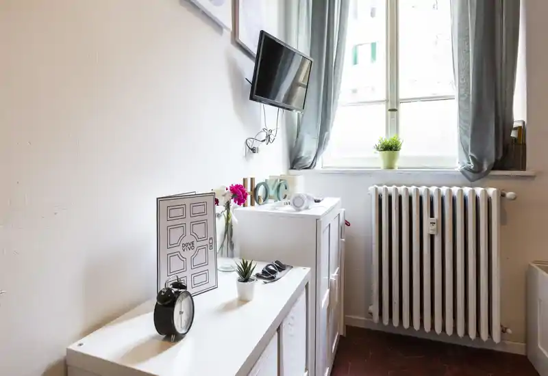 Angolo living luminoso con TV a parete, mobili decorativi e luce naturale dalla finestra; piante e fiori aggiungono un tocco accogliente.