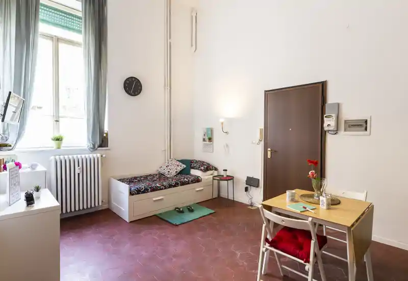 Estudio compacto y luminoso con una cama tipo daybed individual, mesa de comedor y una gran ventana que proporciona luz natural — ideal para estancias cortas y acogedoras.