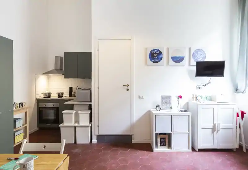 Zona de estar luminosa y ordenada con cocina compacta, TV en la pared y armarios de almacenamiento — perfecta para un estudio acogedor.