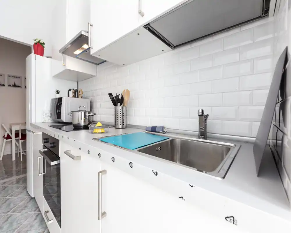 Bright modern kitchen close-up with a stainless sink, induction hob, white cabinets and subway-tile backsplash; compact, clean and well-equipped for short stays.