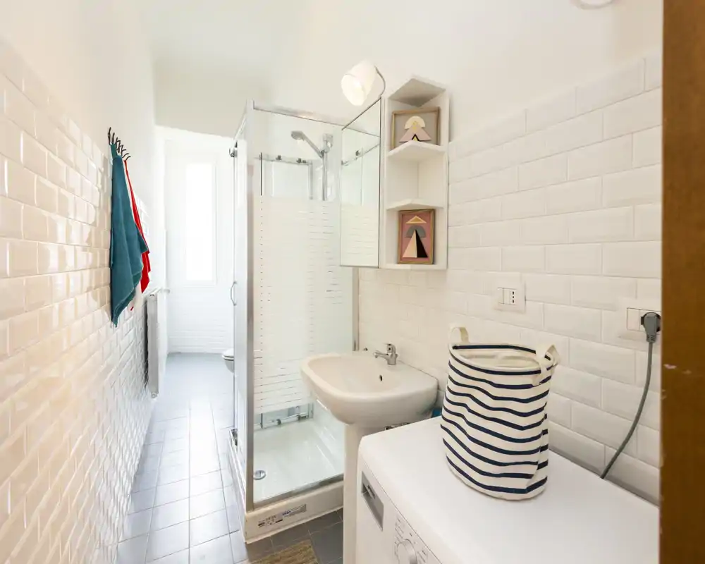 Compact, modern bathroom with a glass shower enclosure, wall-mounted sink, washing machine and bright white tiles creating a clean, fresh feel.
