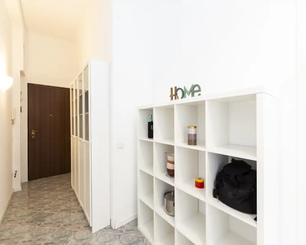 Bright, minimalist entrance hallway with white shelving and a wooden entry door — neat storage and clean lines ideal for welcoming guests.