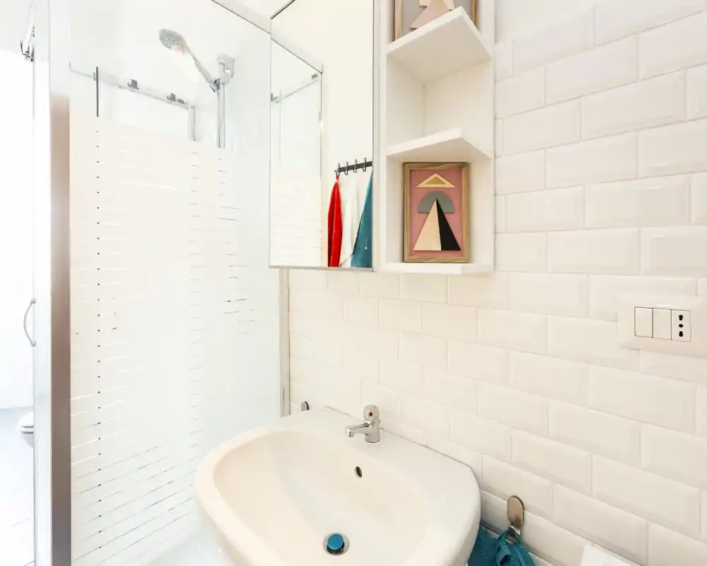 Bright, modern bathroom with a sink, mirror cabinet and a glass shower enclosure. White subway tiles and neat storage create a clean, fresh atmosphere.