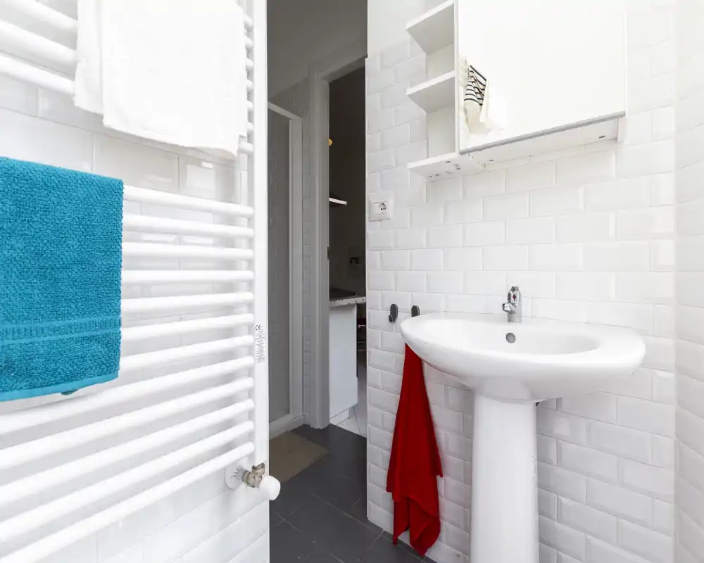 Bagno moderno e luminoso con piastrelle bianche effetto subway, lavabo a colonna e scaldasalviette. Spazio pulito e ben illuminato, ideale per annunci.