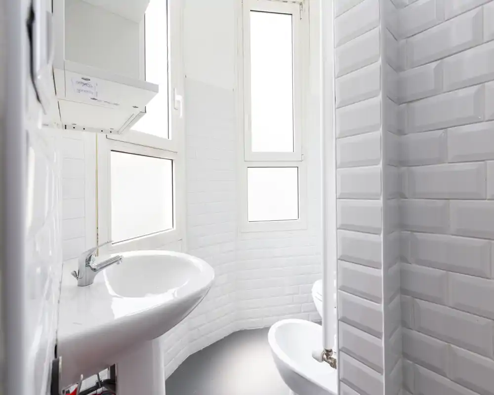 Bagno compatto e luminoso con piastrelle bianche effetto subway, lavabo a colonna e bidet; luce naturale morbida dalle finestre con vetro satinato.